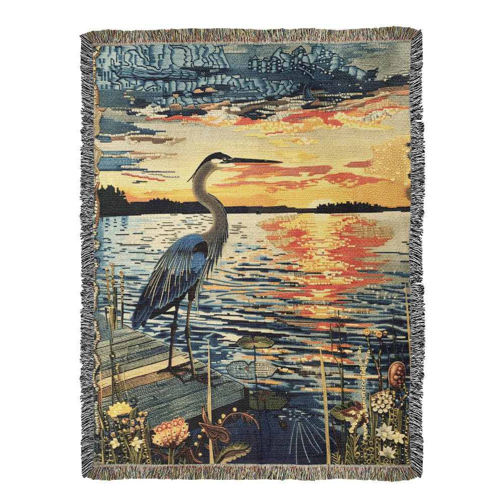 A woven blanket featuring a central heron with outstretched wings against a sunset background, laid out on a floor with decorative elements around.